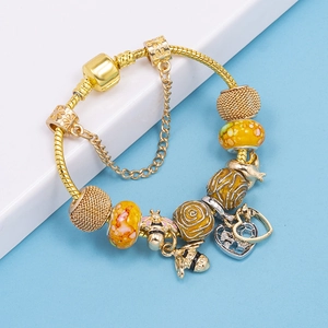 Goldenes Schlangenarmband mit Bienen-Anhängern und gelben Glasperlen auf blauem Grund