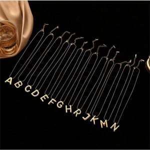 Polished gold 3D initial letter necklaces displayed on premium black velvet background