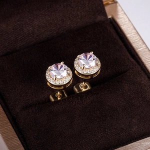 Close-up of elegant gold stud earrings with round brilliant zircon and halo setting