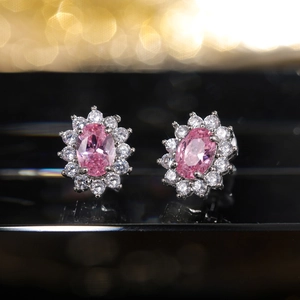 Macro close-up of pink oval zircon earrings with a halo of white stones on a black mirror