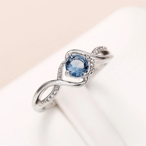 Macro shot of silver wavy ring with blue zircon center stone and diamond accents