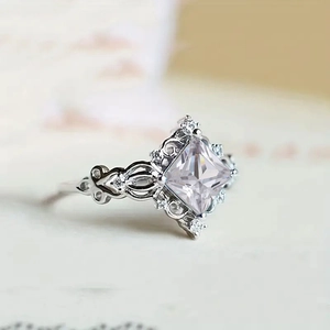 Macro shot of silver ring featuring princess-cut gemstone and hollow lace detailing