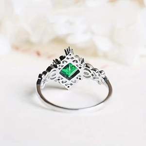 Macro detail of silver ring featuring square green gemstone and intricate hollow carvings