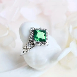 Detailed macro view of vintage emerald cut green gemstone ring with hollow silver patterns