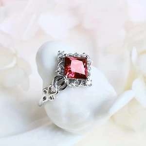 Macro view of vintage silver ring featuring a princess-cut red gemstone and filigree details