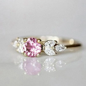 Détails d'une bague dorée ornée d'une pierre rose ronde et de diamants blancs marquises