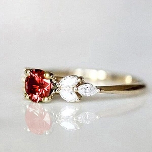 Gros plan d'une bague dorée avec pierre rouge ronde et pierres blanches marquises sur le côté