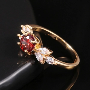 Gros plan d'une bague dorée avec gemme rouge et accents marquise sur fond noir poli