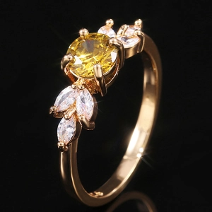 Détail d'une bague avec gemme jaune ronde et pierres en feuilles sur fond sombre