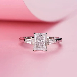 Macro shot of rectangular radiant cut crystal ring with side stones on pink background