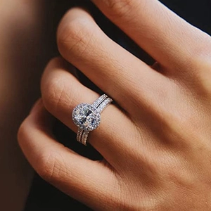 Detail eines ovalen Halo-Verlobungsring-Sets mit Pavé-Steinen an der Hand