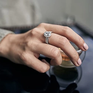 Nahaufnahme eines luxuriösen Halo-Diamantrings an der Hand des Models mit Teetasse