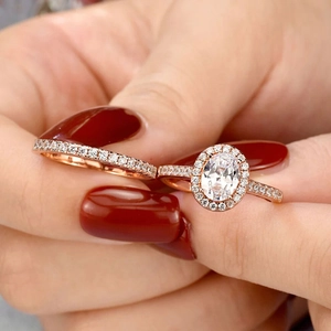 Nahaufnahme von Eheringen in Roségold mit ovalem Halo-Verlobungsring und Pavé-Band