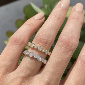 Close-up of gold and silver bezel-set eternity bands with round stones stacked on a finger