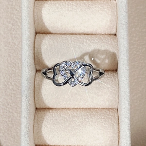 Macro detail of silver heart and infinity ring with pave cubic zirconia on beige velvet