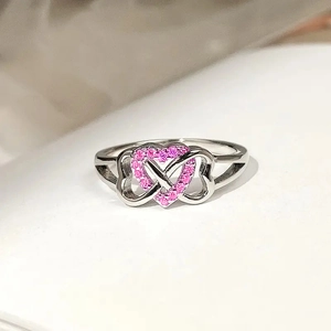 Detail of silver ring with three hearts and pave-set pink zircons on a white surface