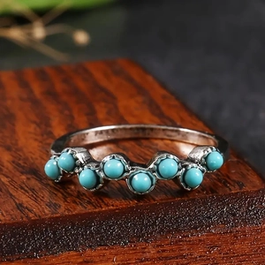 Détail macro de la bague ondulée avec sept perles turquoise sur base en bois foncé
