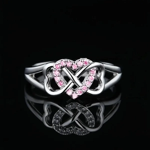 Macro shot of silver ring with pink pavé heart and infinity symbol on black background