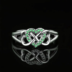 Macro shot of silver ring featuring green gemstones on heart and infinity design