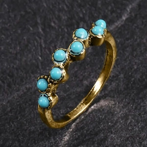 Vue détaillée d'une bague vague dorée avec sept perles turquoise sur une surface en pierre