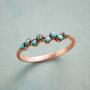 Détail d'une bague en or rose avec sept pierres turquoise en forme de vague