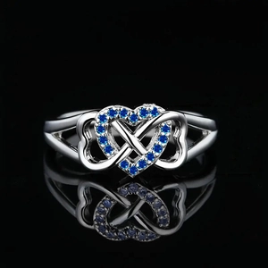 Silver infinity heart ring with blue zircon stones on a reflective black background