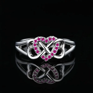 Infinity heart ring with pink pavé gemstones in silver finish against a dark reflection
