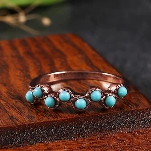 Vue latérale macro d'une bague ondulée or rose avec perles turquoise sur bois