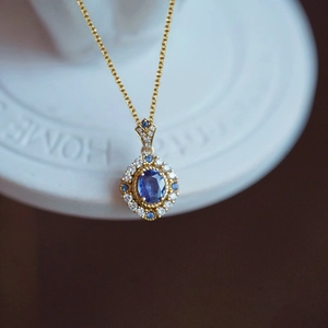 Vintage royal style gold necklace featuring an oval blue sapphire pendant with diamond halo