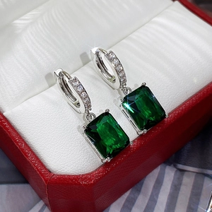 Macro detail of emerald-cut green stone earrings with silver-tone micro-pave setting