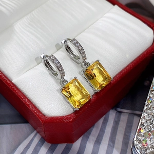 Detailed macro view of silver hoop earrings with rectangular yellow zircon in a gift box