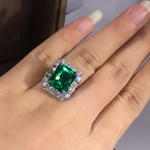Detail of luxury emerald cut green gemstone ring with halo diamond setting on hand