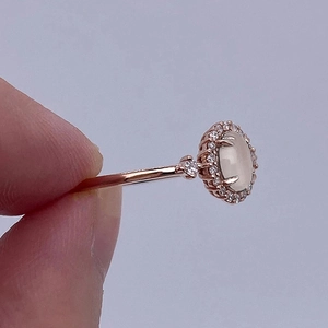 Elegant rose gold oval cabochon ring with moonstone-like gem and diamond halo