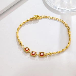 Detail view of 18K gold bamboo link bracelet with three square-cut red gemstones