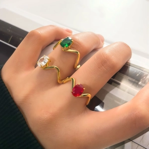 Trois bagues dorées ondulées serties d'émeraude, de rubis et de pierres ovales étincelantes