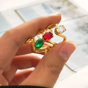 Détail macro de trois bagues dorées ondulées serties d'émeraude, rubis et pierres zircons
