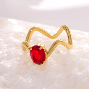 Détail d'une bague dorée ondulée avec une pierre précieuse rouge ovale sertie de quatre griffes
