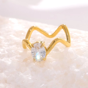Gros plan d'une bague dorée ondulée avec pierre de cristal ovale sur texture blanche