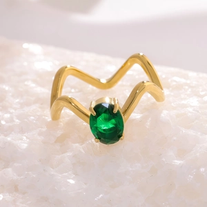 Détail d'une bague dorée ondulée ornée d'une pierre précieuse verte de forme ovale
