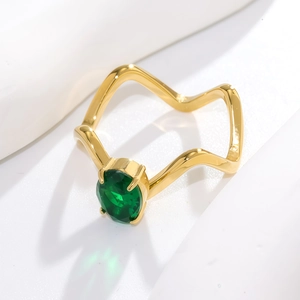 Détail d'une bague dorée ondulée avec pierre ovale vert émeraude sertie à quatre griffes
