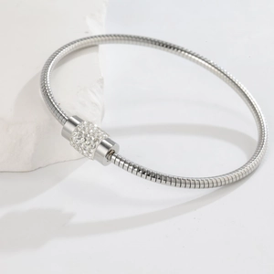 Close-up of silver snake chain bracelet featuring a round clasp pave-set with white crystals
