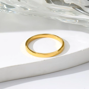 Minimalist gold-plated stainless steel ring shown on white display stand with water ripple background