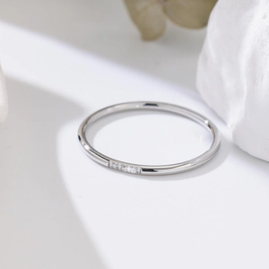 Macro detail of silver minimalist ring with three small inlaid crystals on a white stone