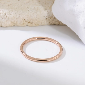 Gros plan d'une bague minimaliste en or rose de 1,5 mm sur un support en pierre blanche