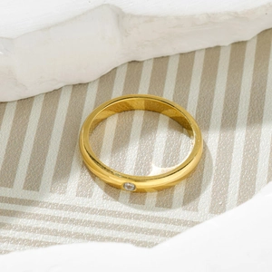 Polished gold titanium steel ring with a small sparkling diamond on a stone background