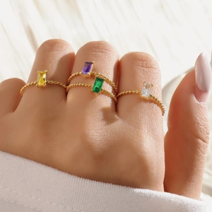 Detailed view of stacked gold twisted rings with colorful rectangular gemstones on finger