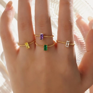 Detail of four stackable gold twist rings featuring colorful rectangular gemstones on hand