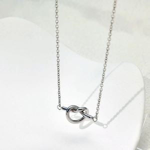 Collier élégant avec pendentif nœud en acier titane sur un support en céramique blanc