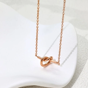 Collier minimaliste en titane or rose avec pendentif nœud sur un support décoratif