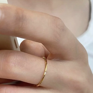 Close-up of minimalist thin gold ring featuring a small square diamond on a finger